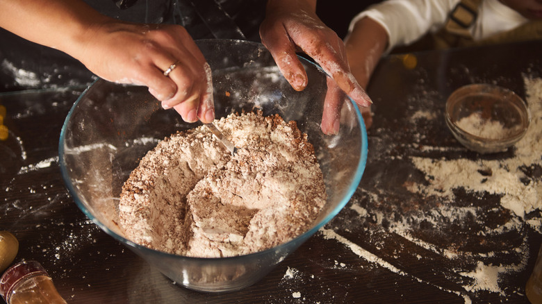Person mixing ingredients in a glass bowl.