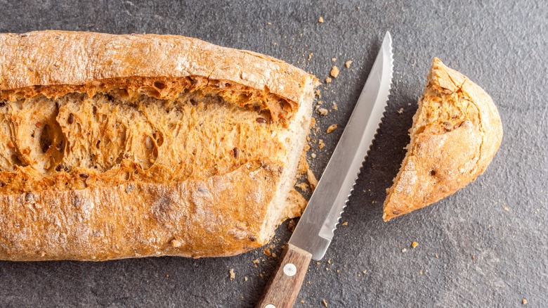 A loaf of bread with the heel cut off and a serrated knife between the heel and loaf