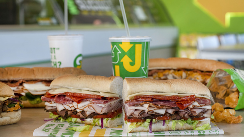 Subway meat lover's sandwiches and soft drinks on table.