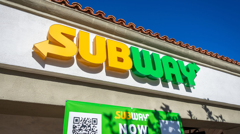 Subway restaurant exterior sign against blue sky.