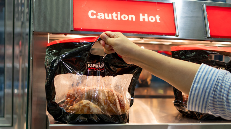 A hand holding up a bag containing a Kirkland Signature rotisserie chicken