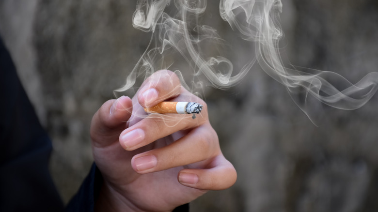 close up of hand holding half lit cigarette