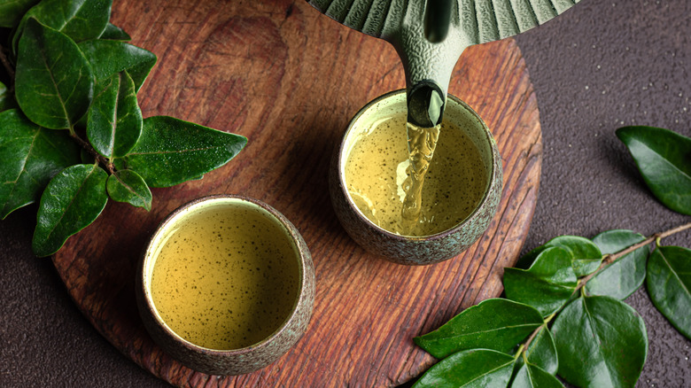 Top view of green tea being poured into a mug from a tea kettle.