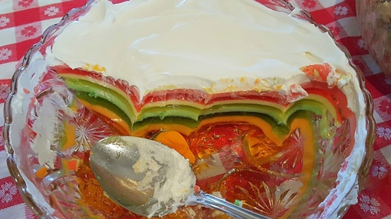 A half-eaten, layered Jell-O salad in a glass bowl with a serving spoon