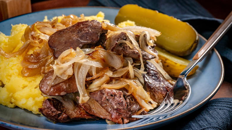 Liver and onions on a blue plate with potatoes and a pickle