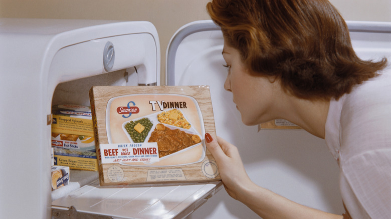 A woman with a 50s hairstyle pulling a Swanson TV dinner from an old-school fridge