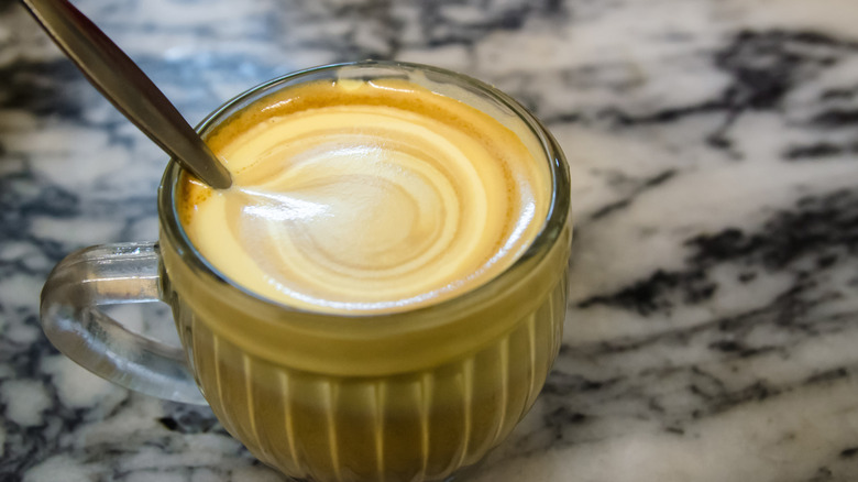 A coffee made with egg yolk in a glass espresso mug with a spoon in it