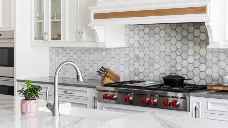 A sink in a kitchen island in front of stove and marble backsplash