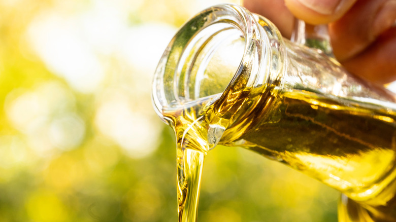 close-up of green olive oil being poured out of a glass bottle and blurred green background
