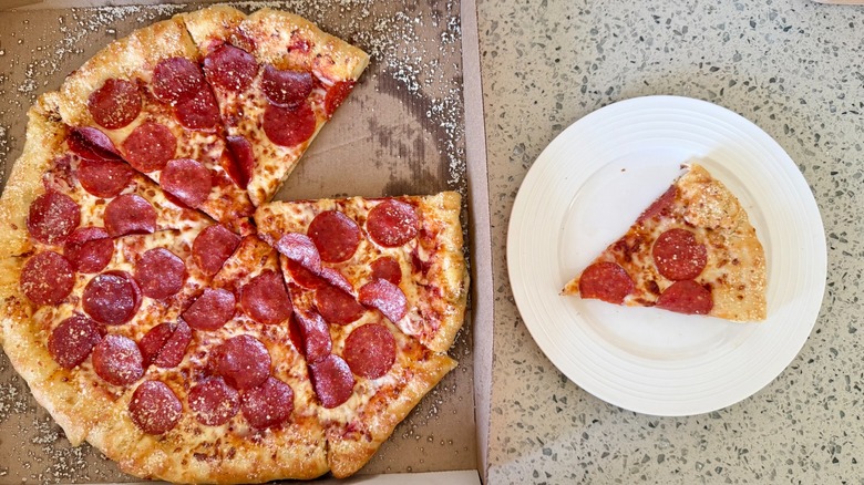 A Little Caesars Stuffed Crazy Crust Pepperoni pizza sits on a counter with one slice on a plate next to it.