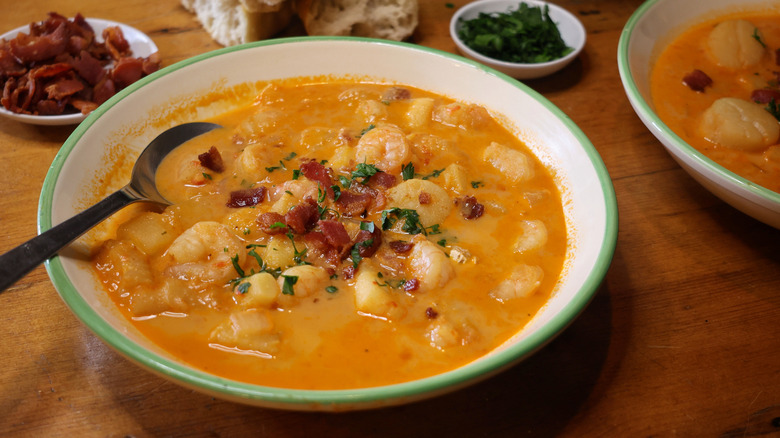 a bowl of Long Island seafood chowder garnished with parsley and bacon on a wooden table