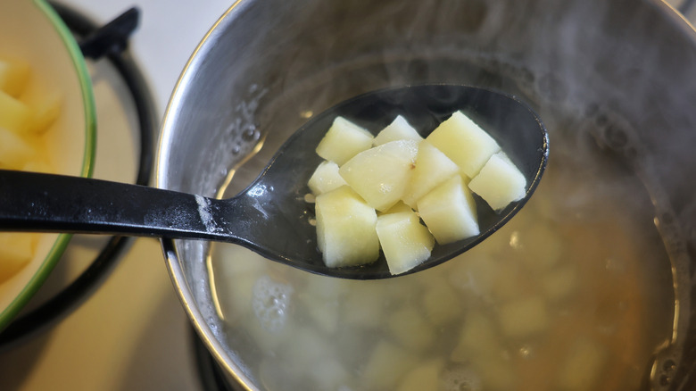 diced potatoes being lifted from a pot of boiling water with a slotted spoon