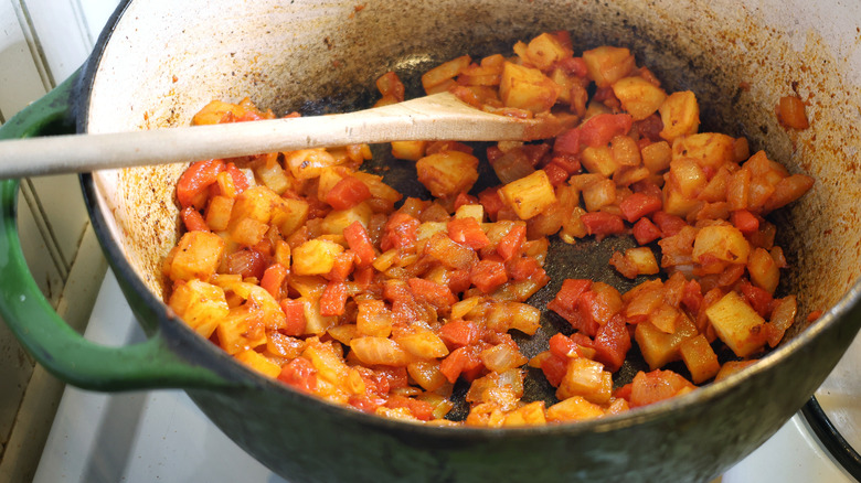 a pot of diced potatoes, onions, and roasted red peppers coated in tomato paste with a wooden spoon in it
