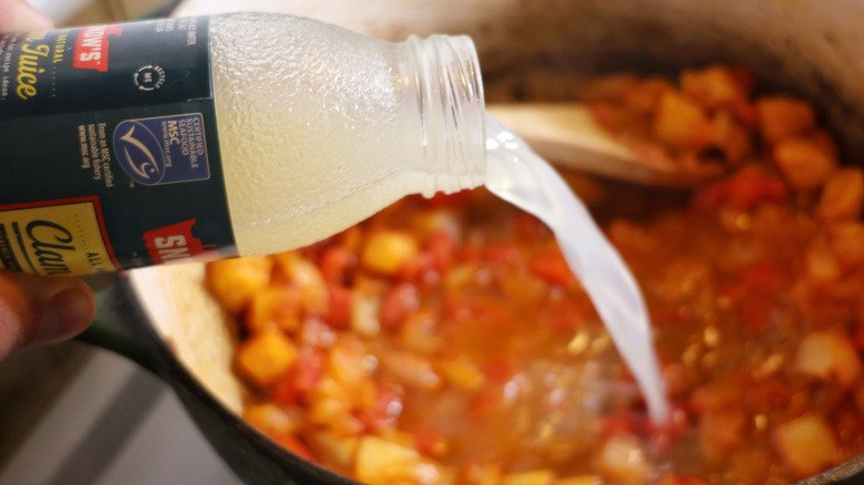 clam juice pouring from the bottle into a pot of vegetables