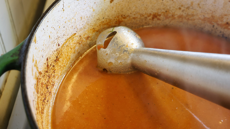 an immersion blender in a pot of orange-red liquid