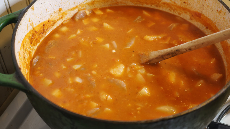 a pot of orange-red seafood stew with a wooden spoon in it