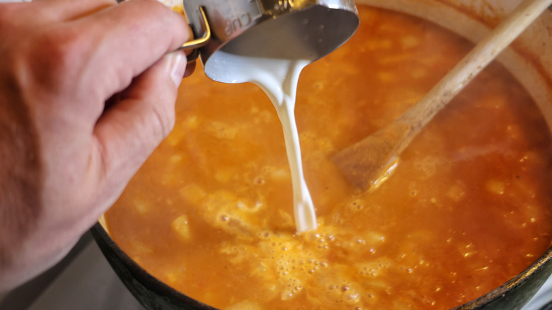 cream pourig from a measuring cup into a pot of Long Island seafood chowder