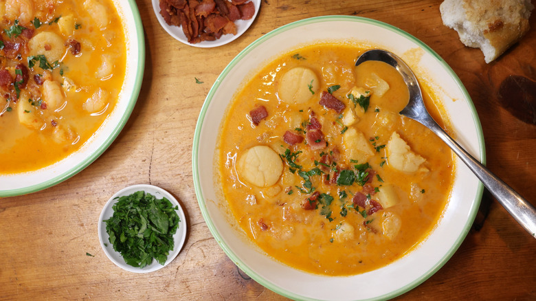 overhead view of two bowls of Long Island seafood chowder garnished with bacon and parsley on a wooden table with bread, bacon, and parsley nearby