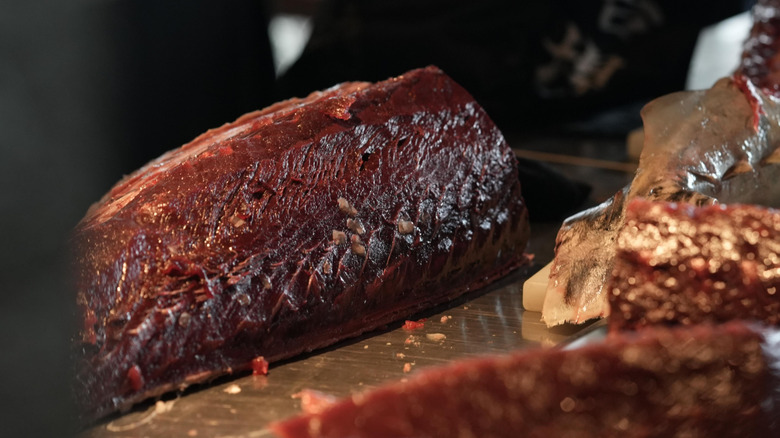 a very dark cut of raw tuna bloodline on a table with other cuts of fish
