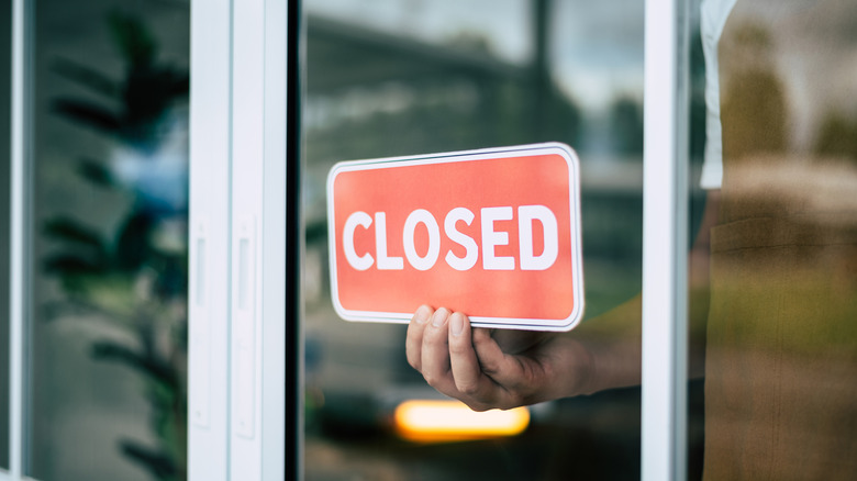 A person affixing a red closed sign on the inside of a window