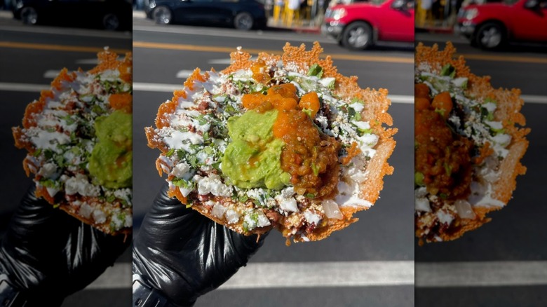 Someone with a black glove holding a queso taco from Villa's Tacos