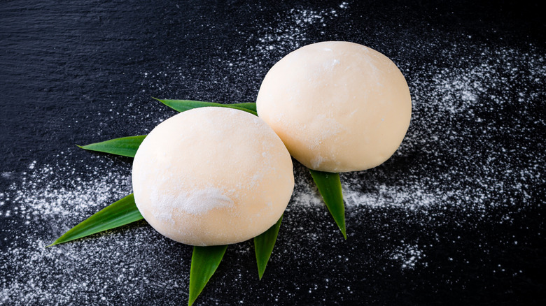 Mochi with leaves and powdered sugar on dark surface