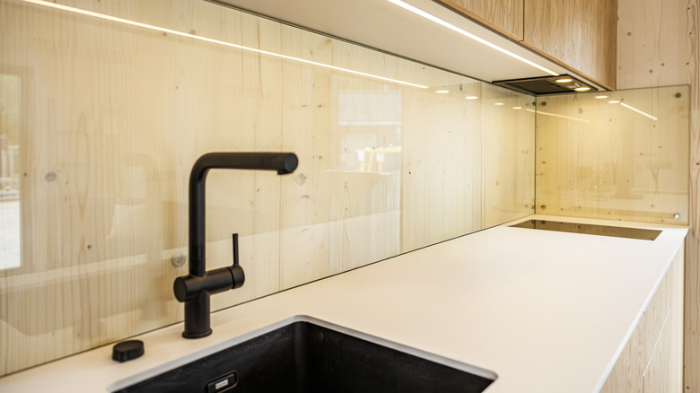 Sink area with wooden walls, glass backsplash, and black faucet