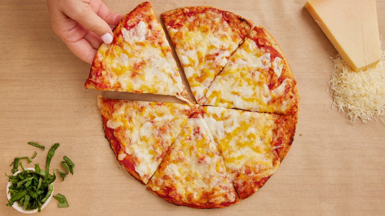 A woman's hand reaching for a slice of a four-cheese pizza