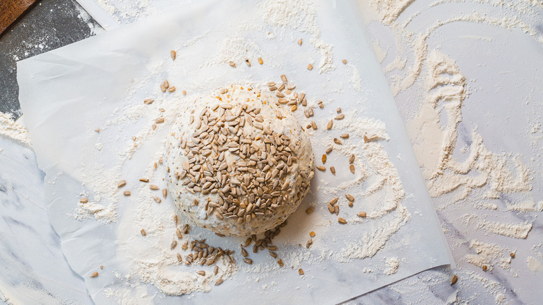 Seed covered dough on parchment with flour alongside bench scraper