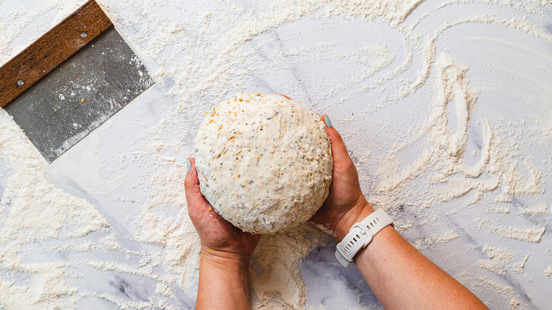 Hands holding dough alongside bench scraper