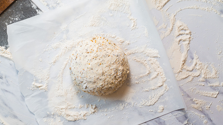 Dough on parchment with flour alongside bench scraper