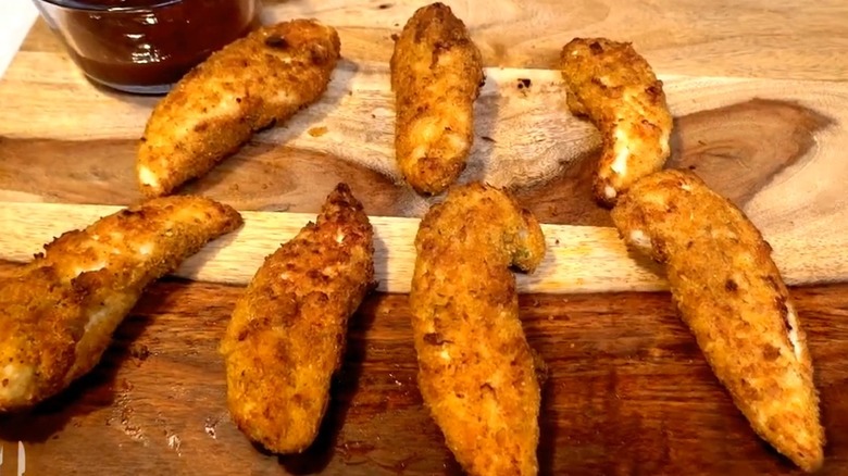 Chicken Tenders lie on a wooden table with dipping sauce nearby