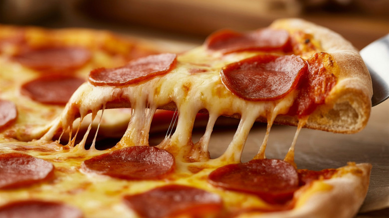 Serving knife lifting slice of pepperoni pizza