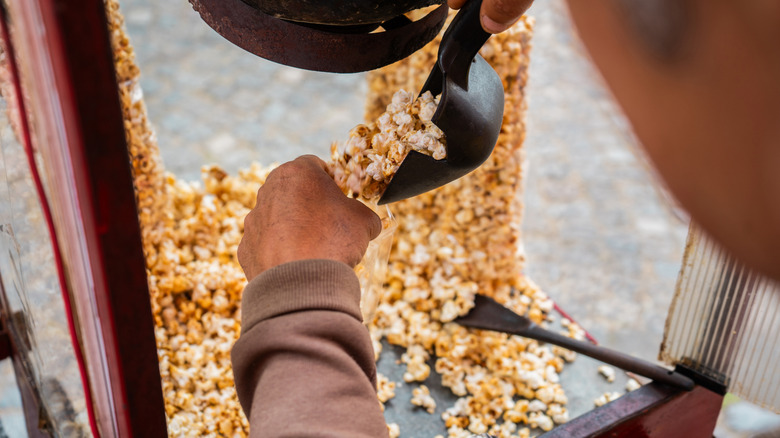 A person pours popcorn into a bag using a scoop.