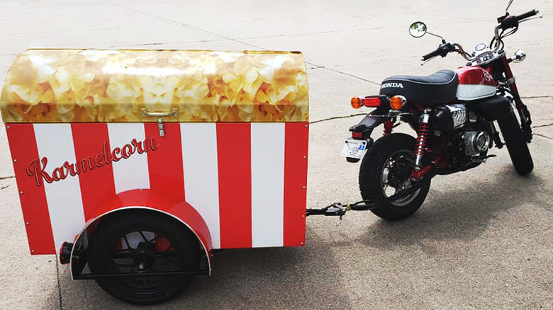 A motorcycle has a Karmelcorn popcorn trailer attached to the back.
