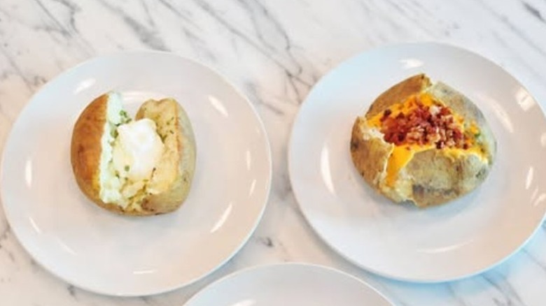Sour cream and chive baked potato on a plate next to another plate with a cheese and bacon baked potato