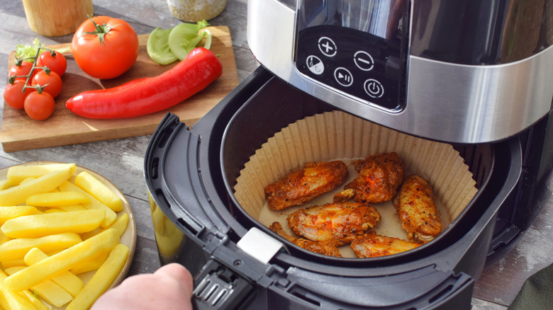 Closeup of person pulling tray of an air fryer basket filled with chicken