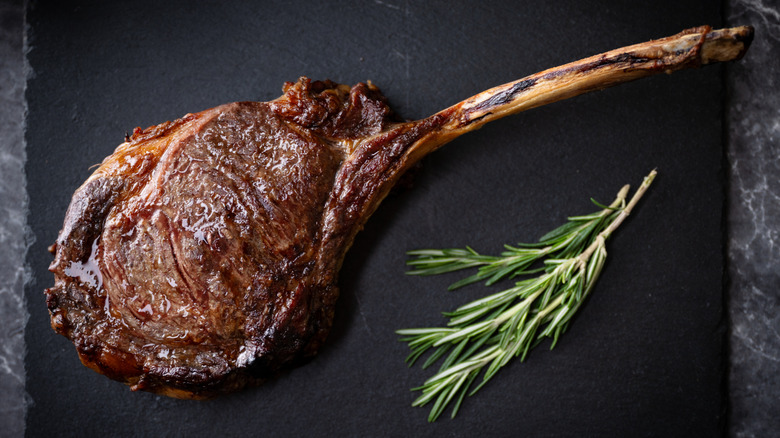 Seared tomahawk steak on a slate board with sprigs of fresh rosemary