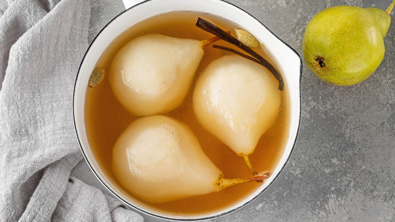 Three poached pears in a dish in their poaching liquid with vanilla and cardamom.