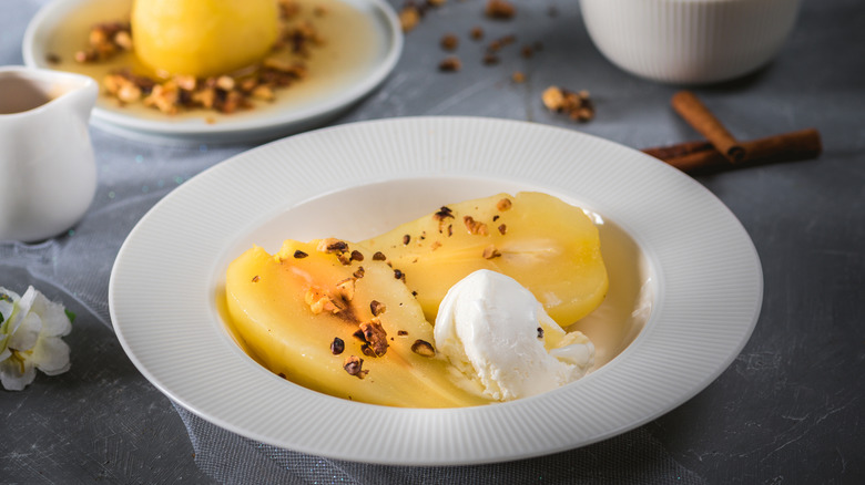 Pears poached in clear liquid served in a dish with ice cream and a sprinkling of chopped nuts.