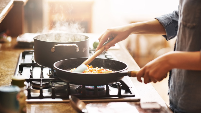Person stirring food in a pan that's placed on the burner.