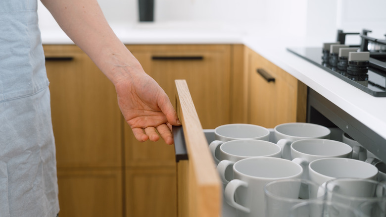 Hand pulling open drawer of mugs