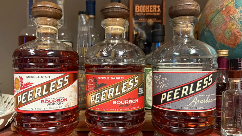 three different bottles of Peerless bourbon lined up next to each other on a wooden desk