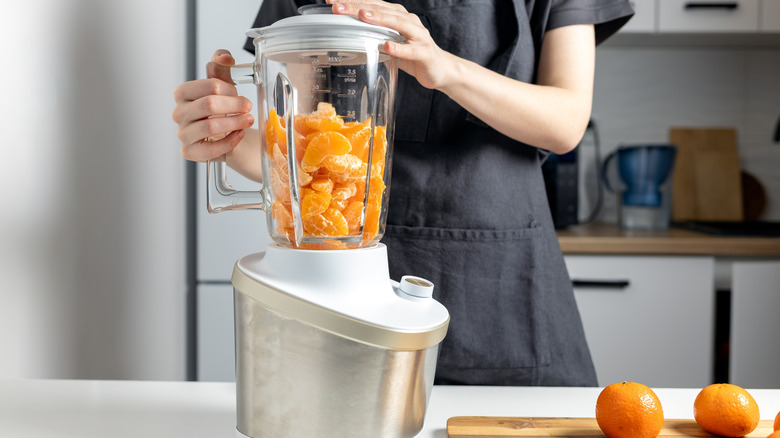 A person making orange juice using a blender.