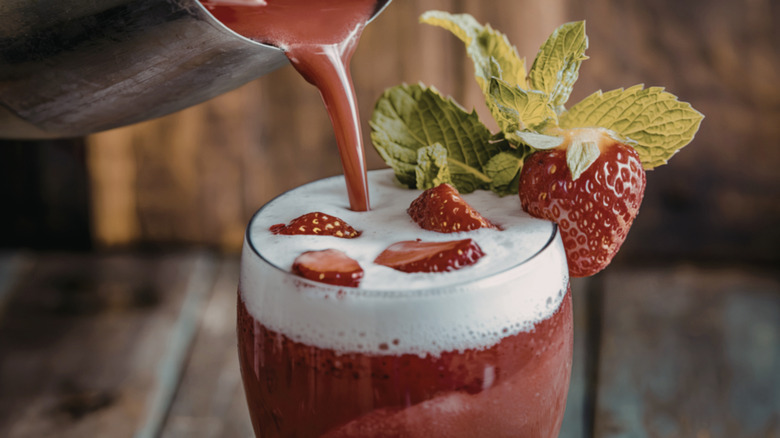 red strawberry cocktail pouring into a glass with mint and berry garnish
