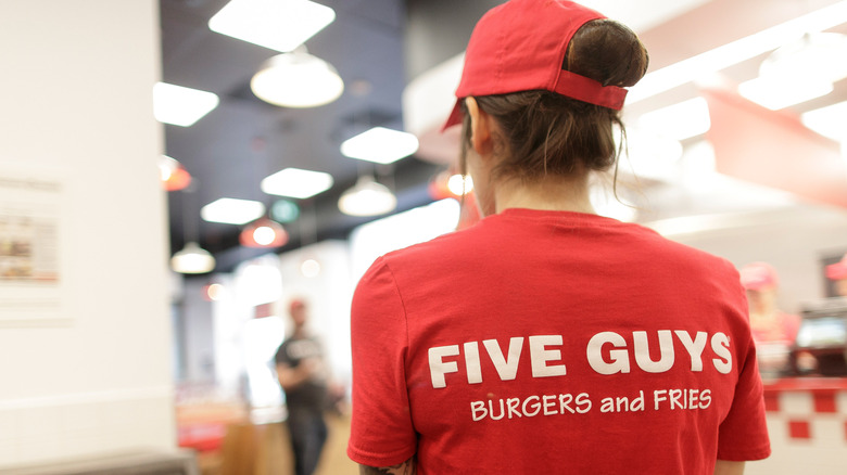 A Five Guys employee wearing a branded t-shirt and hat, seen from the back
