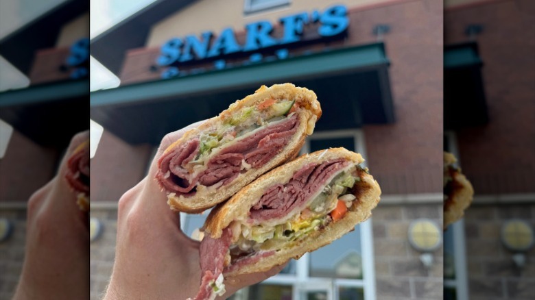 person holding a sandwich in front of Snark's sign