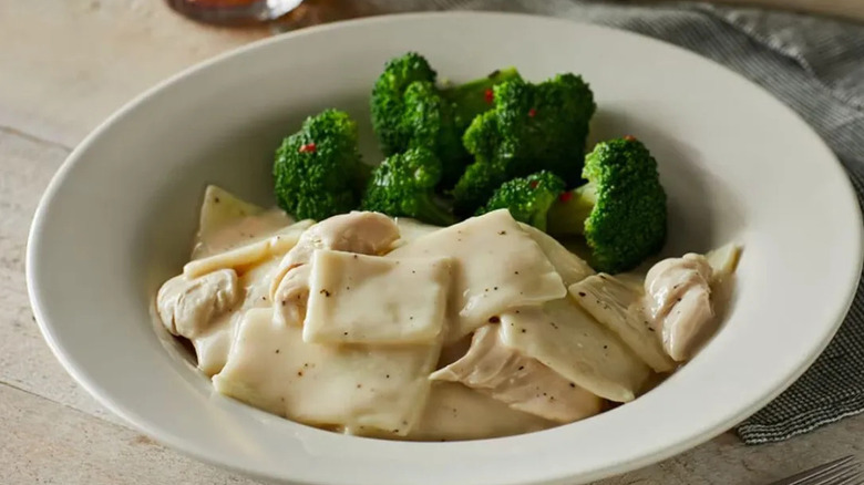 A white bowl of Cracker Barrel chicken and dumplings with a side of broccoli