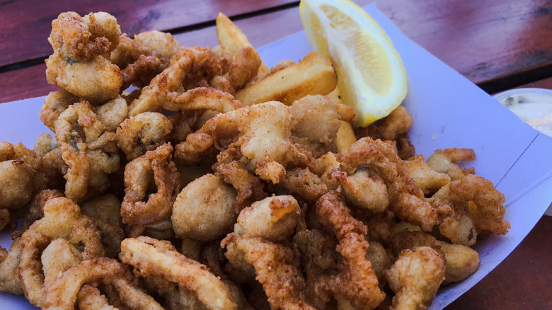 Platter of New England-style fried clams with a lemon wedge on a wooden table