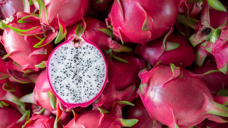Several dragon fruit, one cut in half to expose white flesh